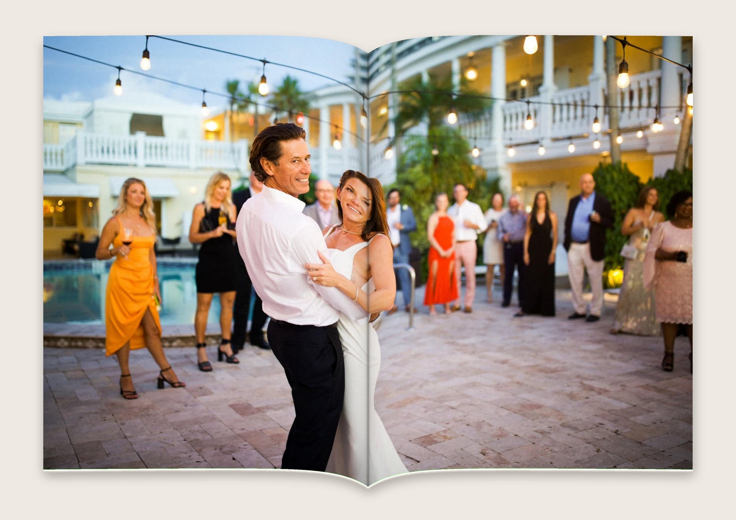 Photograph of a couple dancing in the courtyard under string lights as guests look on.